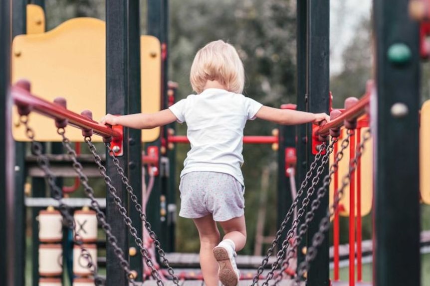 A young girl, pictured from behind, walks along a chain bridge in a children's playground