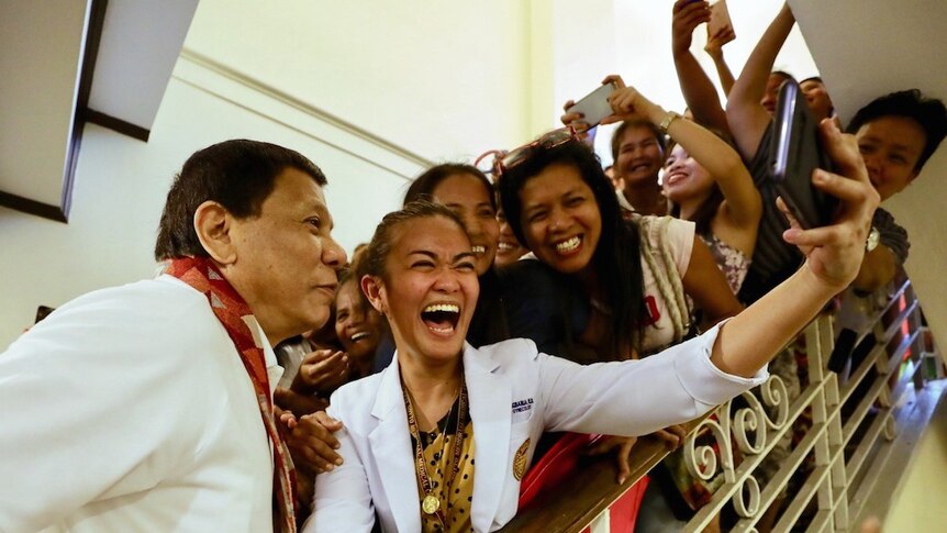 A staircase is full of people holding smartphones in the air trying to get a photo with Rodrigo Duterte.