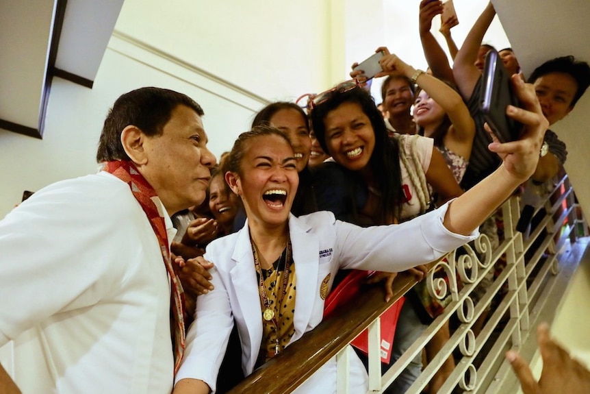 A staircase is full of people holding smartphones in the air trying to get a photo with Rodrigo Duterte.