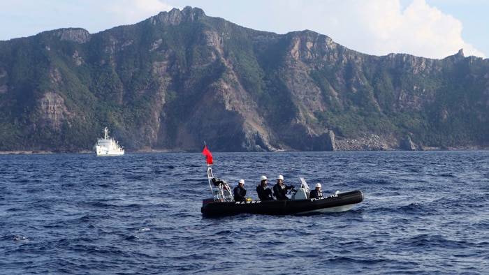 A Japan Coast Guard boat and vessel sail past one of the disputed Senkaku islands