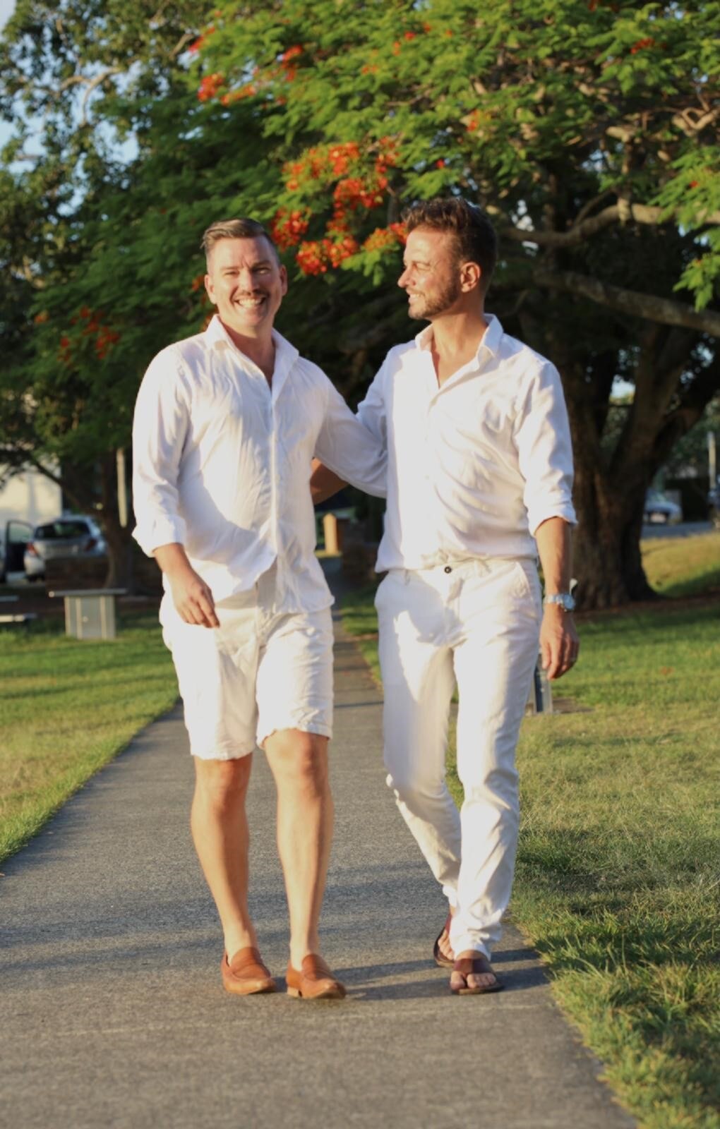 Scott and Brad Harker are dressed in white and walking through a park.