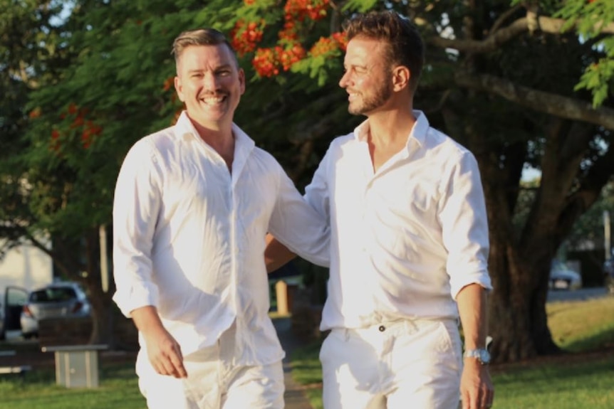 Scott and Brad Harker are dressed in white and walking through a park.