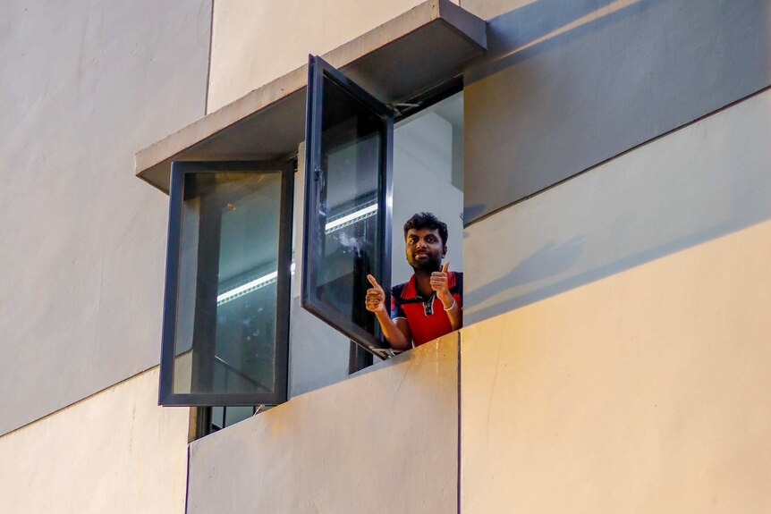 A man in a window gives a thumbs up