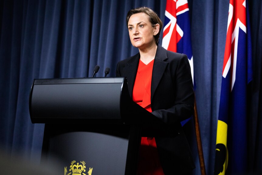 Woman speaks in front of lectern in front of the Australian and Western Australian flag.