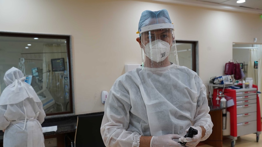 Man wearing PPE gear, mask and face shield in hospital ward.