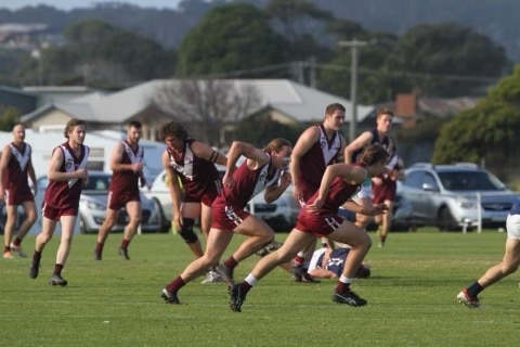 An Australian rules football player on the ground in the background. Several other players are visible. in the foreground