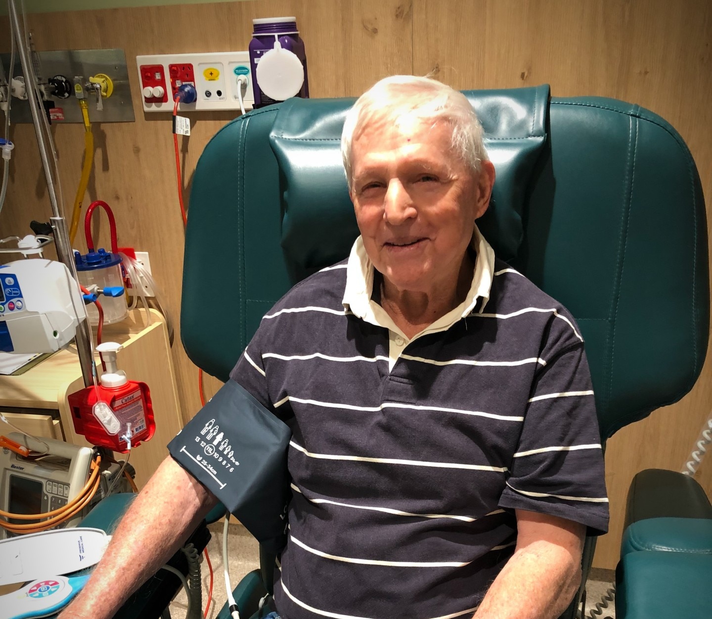 A man sitting in a chair in hospital smiling getting blood pressure taken