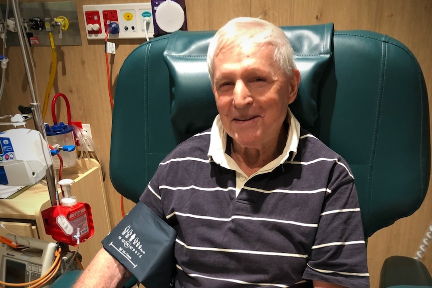 A man sitting in a chair in hospital smiling getting blood pressure taken