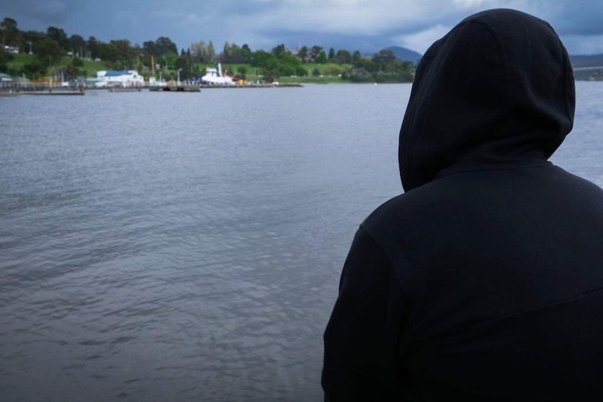 A person wearing a hoodie looks around the water