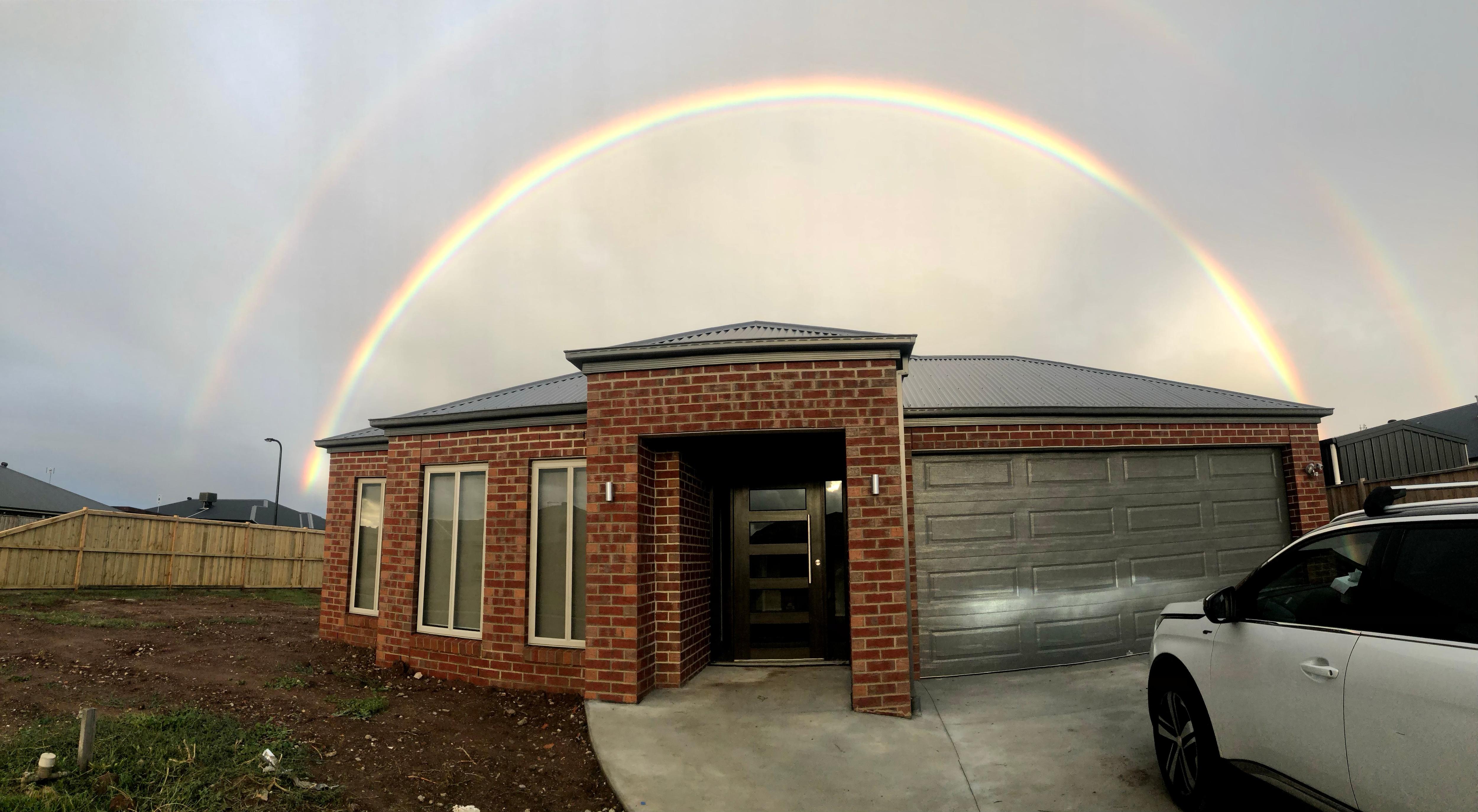 A rainbow shines over a single-storey red brick home.