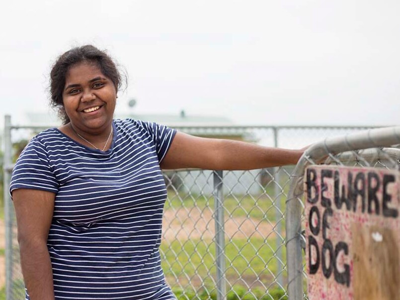 Woman stands with hand on nearby fence, sign on fence reads 'beware of dog'