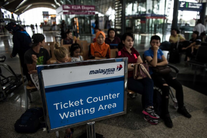 People sit behind Malaysia Airlines sign at Kuala Lumpur Airport
