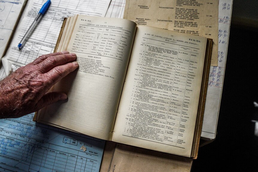 A man's hand rests on an old book listing typed out parcel and luggage items from 1911.