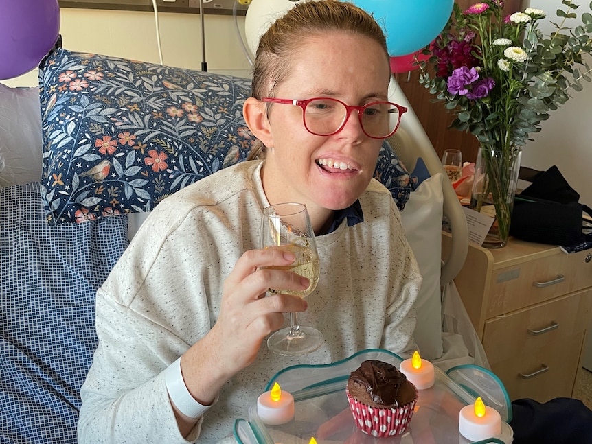 Hannah in hospital on her birthday surrounded by balloons and holding a glass of wine
