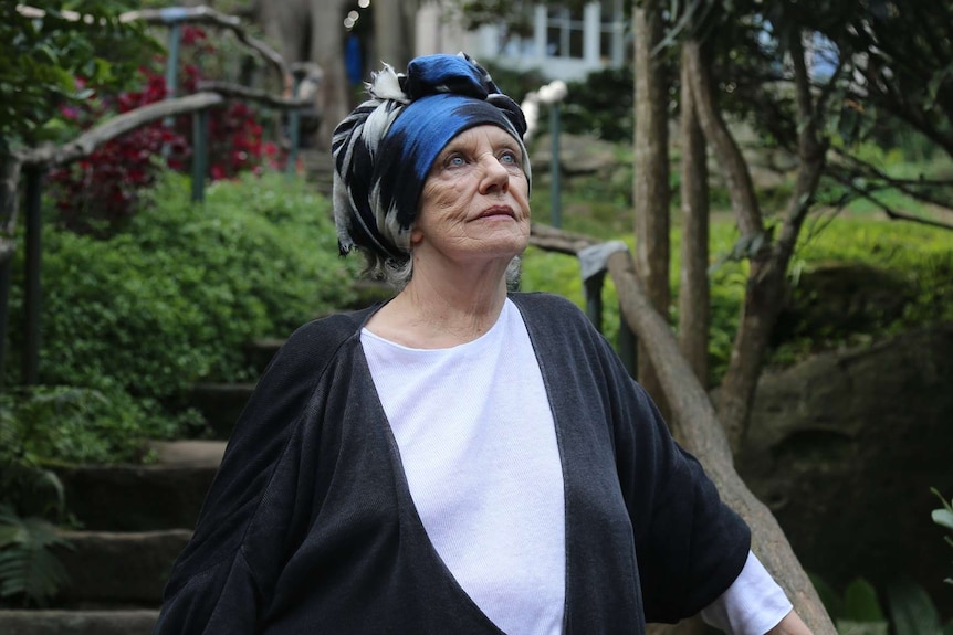 A woman wearing a headscarf stands in a garden.