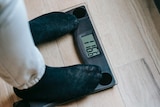 Two feet in black socks stand on a scale, showing 116 kilograms. 