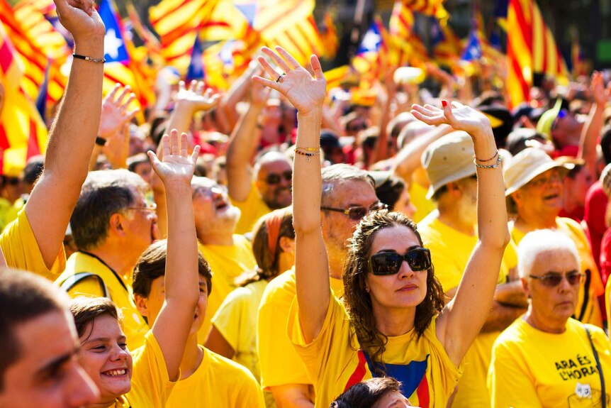 Crowd shot of Catalan independence supporters in Spain, waving flags and dressed in yellow uniforms.