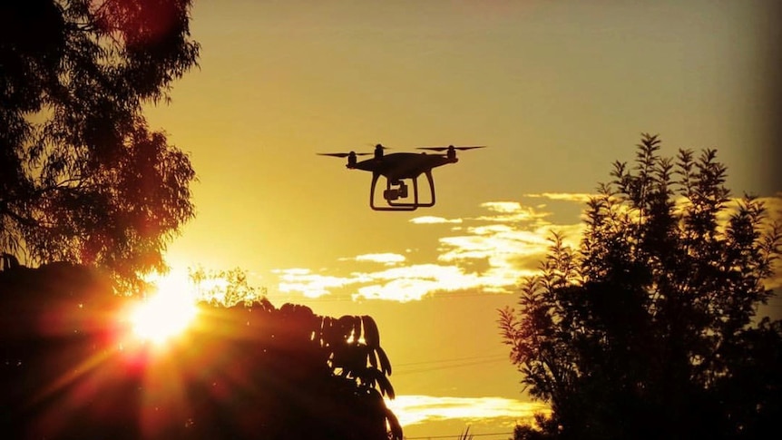 Drone flying in sunset sky over trees, with drone in silhouette, in a Brisbane suburb on October 24, 2018.