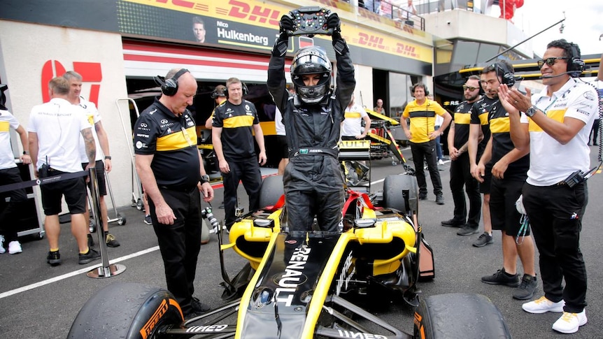 Aseel Al-Hamad holds up the steering wheel, while standing in the Lotus Renault F1 car.