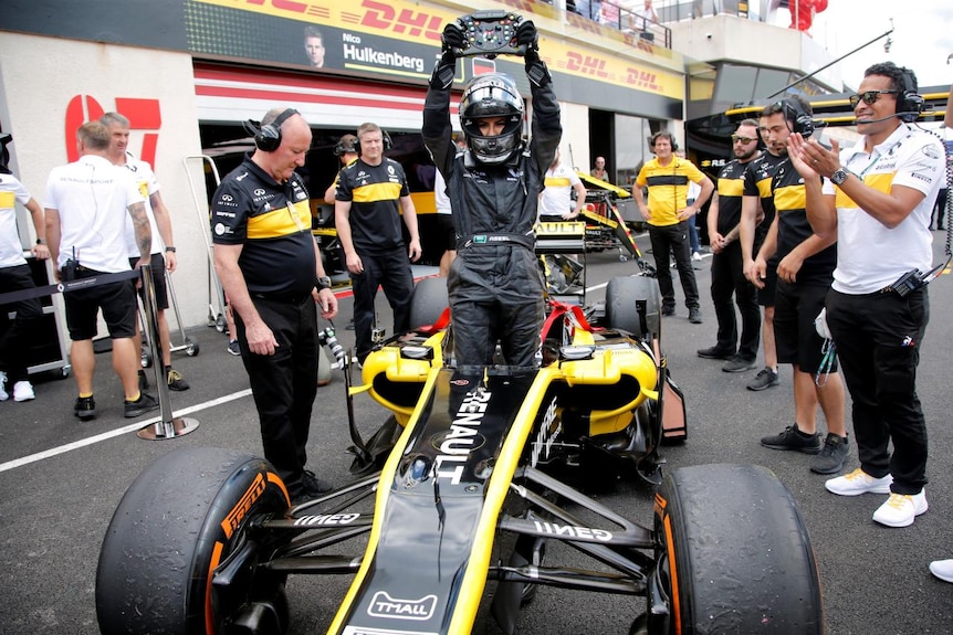 Aseel Al-Hamad holds up the steering wheel, while standing in the Lotus Renault F1 car.