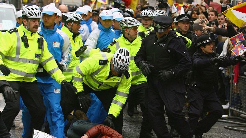 A protester is knocked to the ground by police surrounding the bearer of the Olympic Torch