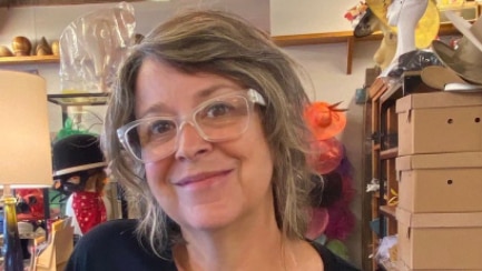 Grey haired woman with clear glasses wearing blue shirt and yellow star patch
