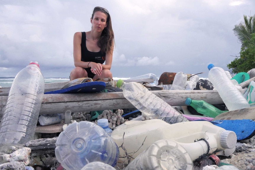 Researcher Jennifer Lavers sitting on a log surrounded by plastic and rubbish on the Cocos (Keeling) Islands.