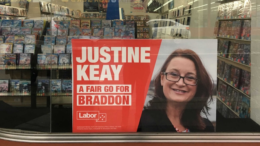 A poster that says "Justine Keay: A fair go for Braddon" with Labor branding sits in the window of a video shop.