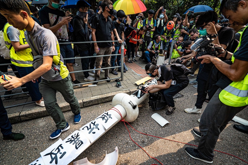 A group of people standing around a white lamppost on the ground with graffiti on it.