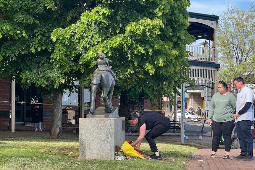 A person lays a floral tribute at the base of a statue on a lawn.