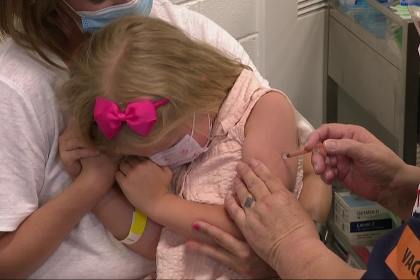A little girl sits in her mum's lap while getting a needle