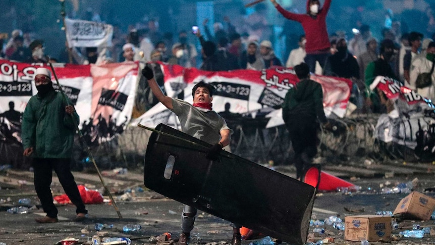 A supporter of Indonesian presidential candidate Prabowo Subianto throws rock at riot police.