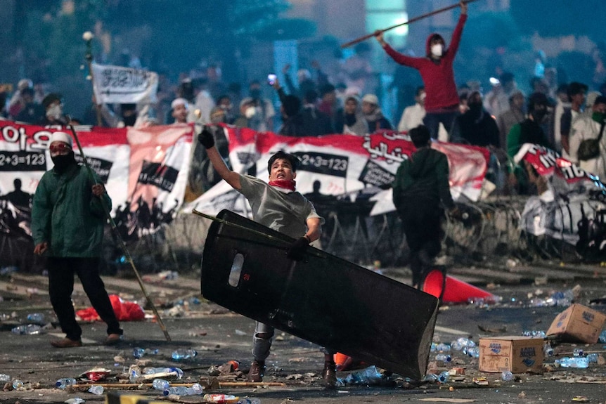 A supporter of Indonesian presidential candidate Prabowo Subianto throws rock at riot police.