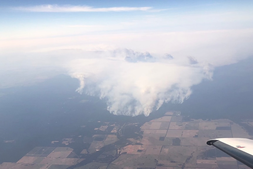 An aerial photo of a smoke rising from a patchwork of agricultural paddocks, a fire burns across the landscape.