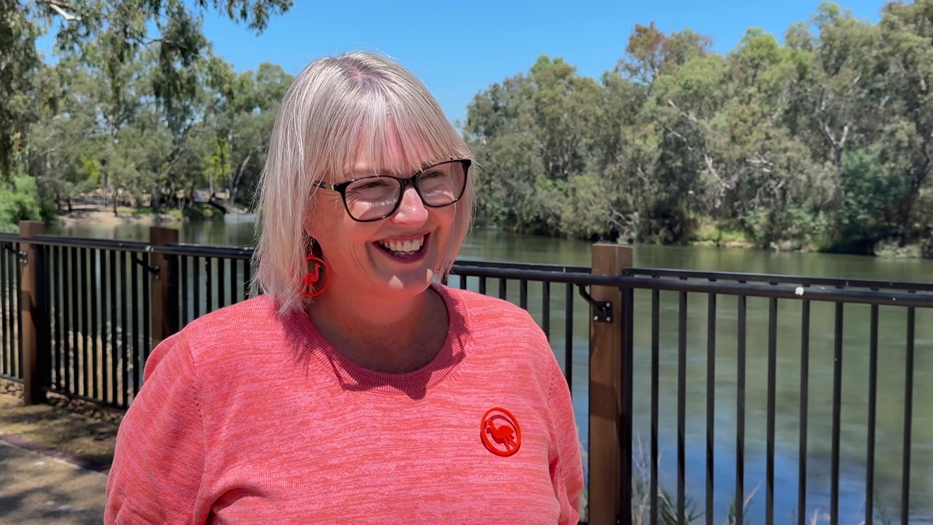 Una mujer con un top rosa sonríe frente a un río. 