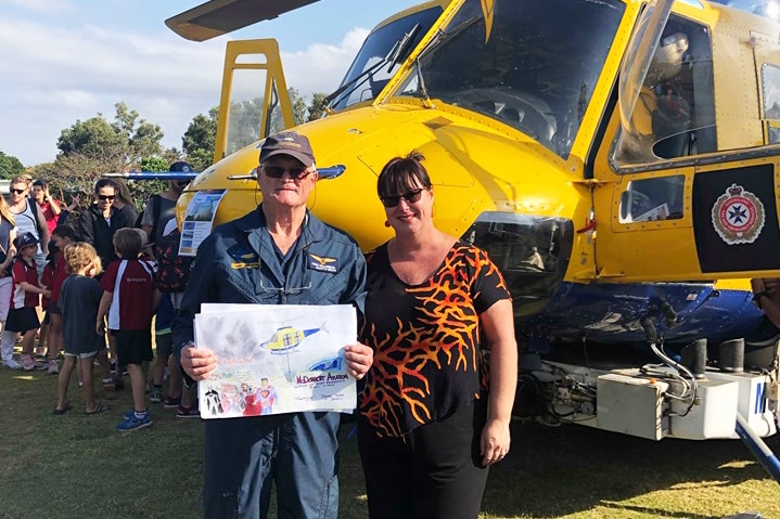 Pilot David Williamson stands next to a woman in front of a helicopter.