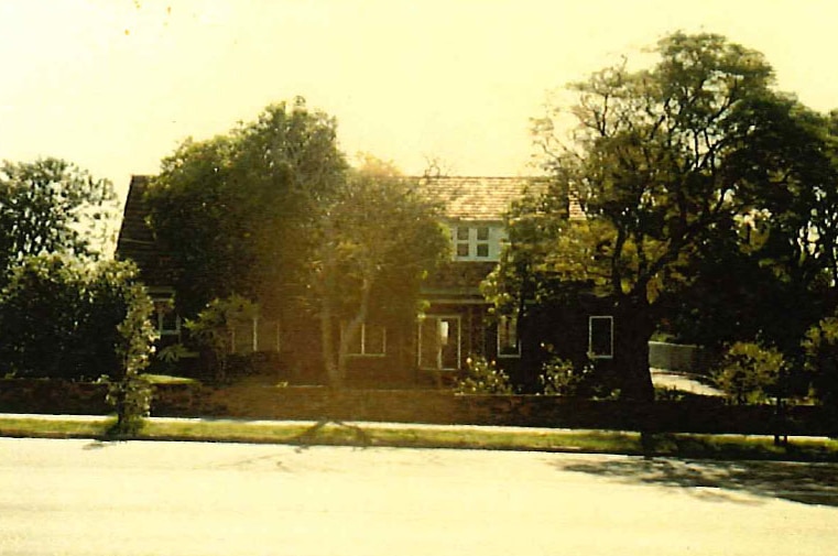 An old photograph of a two story brick house surrounded by trees.