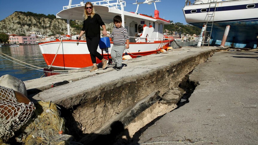 A woman walks down the main habour of Zakynthos with the pavement broken and cracked following an earthquake.