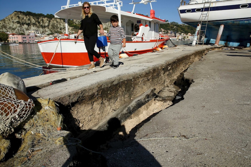 A woman walks down the main habour of Zakynthos with the pavement broken and cracked following an earthquake.