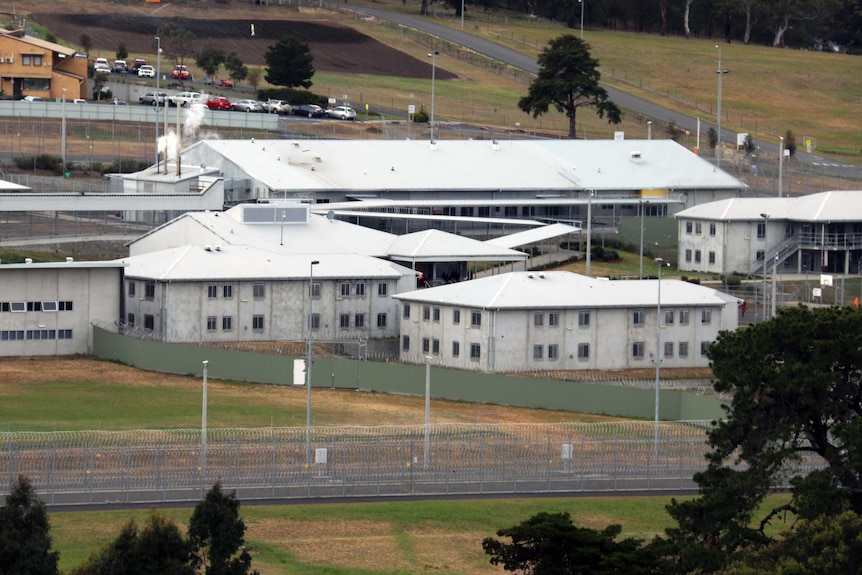 Risdon Prison is seen from beyond an external fence. There are several buildings inside the precinct.