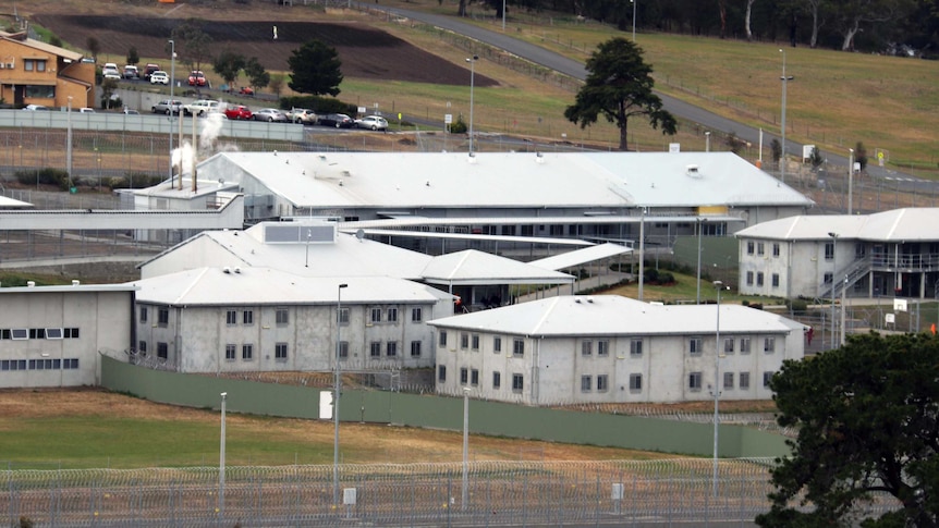 Risdon Prison is seen from beyond an external fence. There are several buildings inside the precinct.