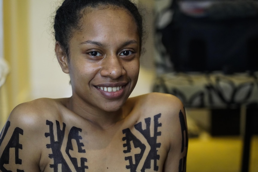 Woman smiling with traditional tattoos on her chest.