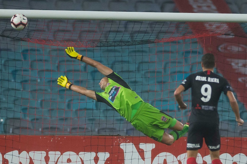 Penalty taken by player goalkeeper diving empty stadium.