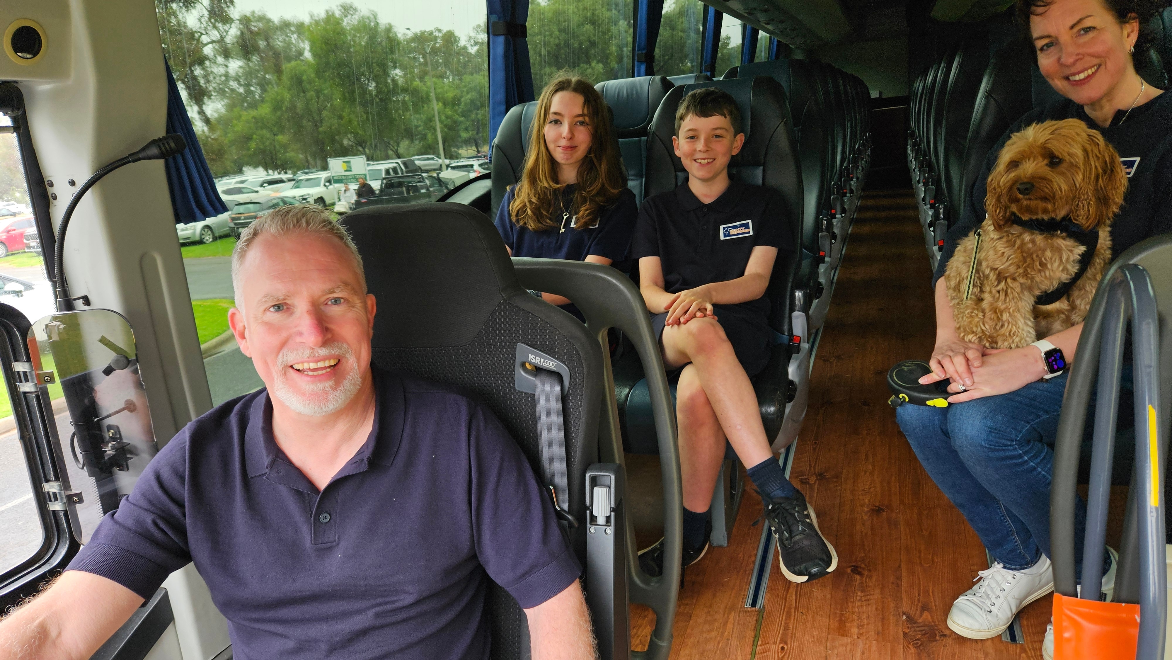 A smiling man in a bus seat, surrounded by his two children, his wife and his dog