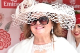 A woman in a large hat and sunglasses smiles broadly.