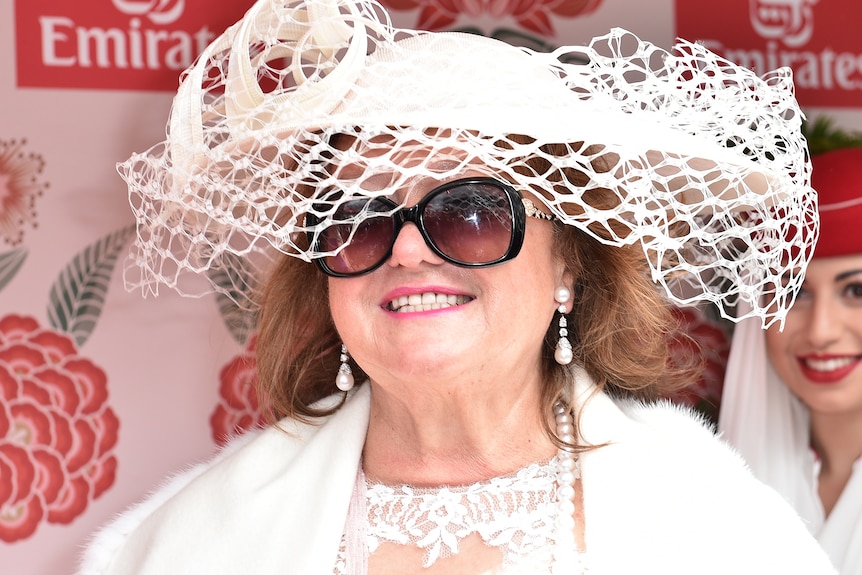 A woman in a large hat and sunglasses smiles broadly.