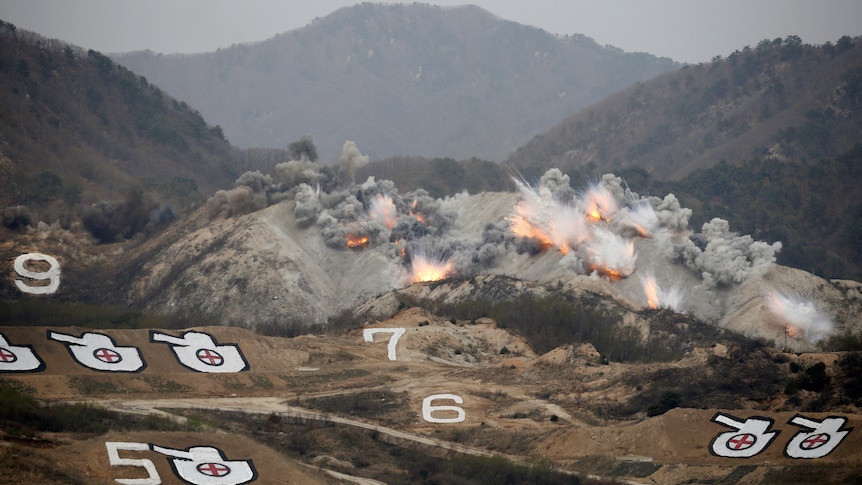 Explosions are seen at a training field dotted with targets in the shape of tanks.