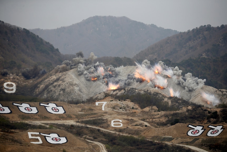 Explosions are seen at a training field dotted with targets in the shape of tanks.