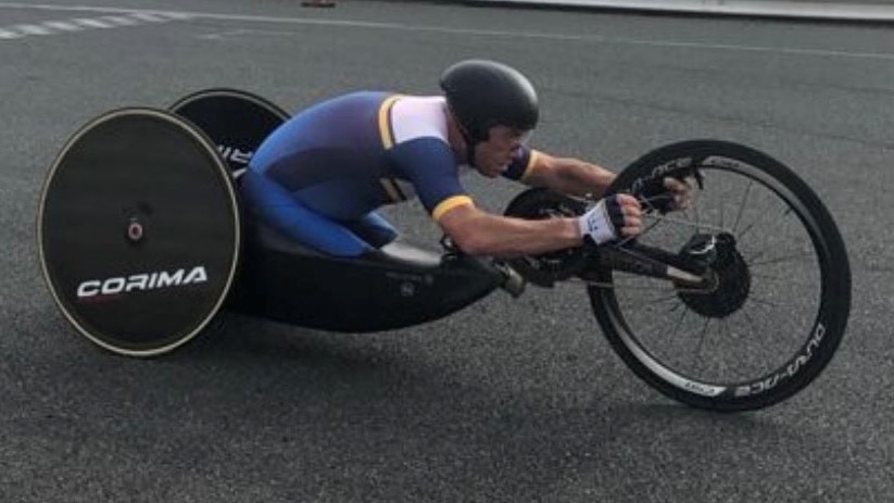 Paralympian cyclist Stuart Tripp on his trike in blue, white and yellow lycra wearing a black helmet.