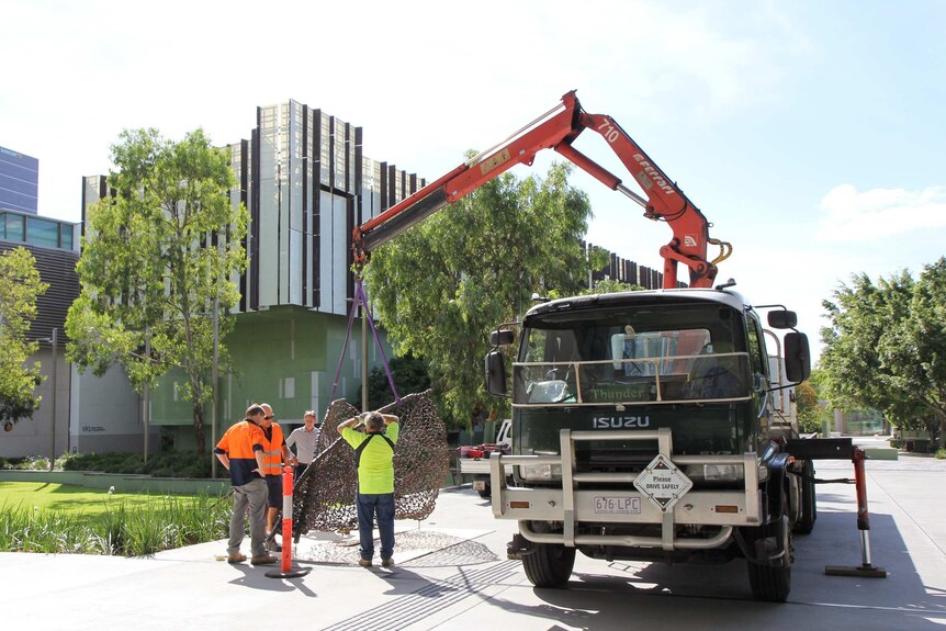 A crane lowers Judy Watson's sculpture, tow row, into position outside GOMA.